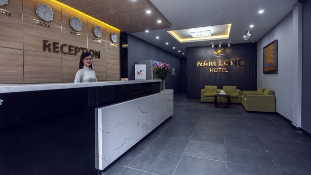 A hotel reception area with a modern design, featuring a reception desk, a clock, and a sign indicating the hotel name. - Nam Long Hotel Ha Noi (Hanoi)