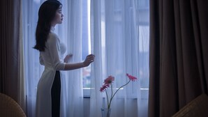 A person standing by a window with sheer curtains, holding a curtain rod. - Nam Long Hotel Ha Noi (Hanoi)