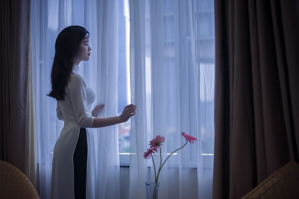 A person standing by a window with sheer curtains, holding a curtain rod.