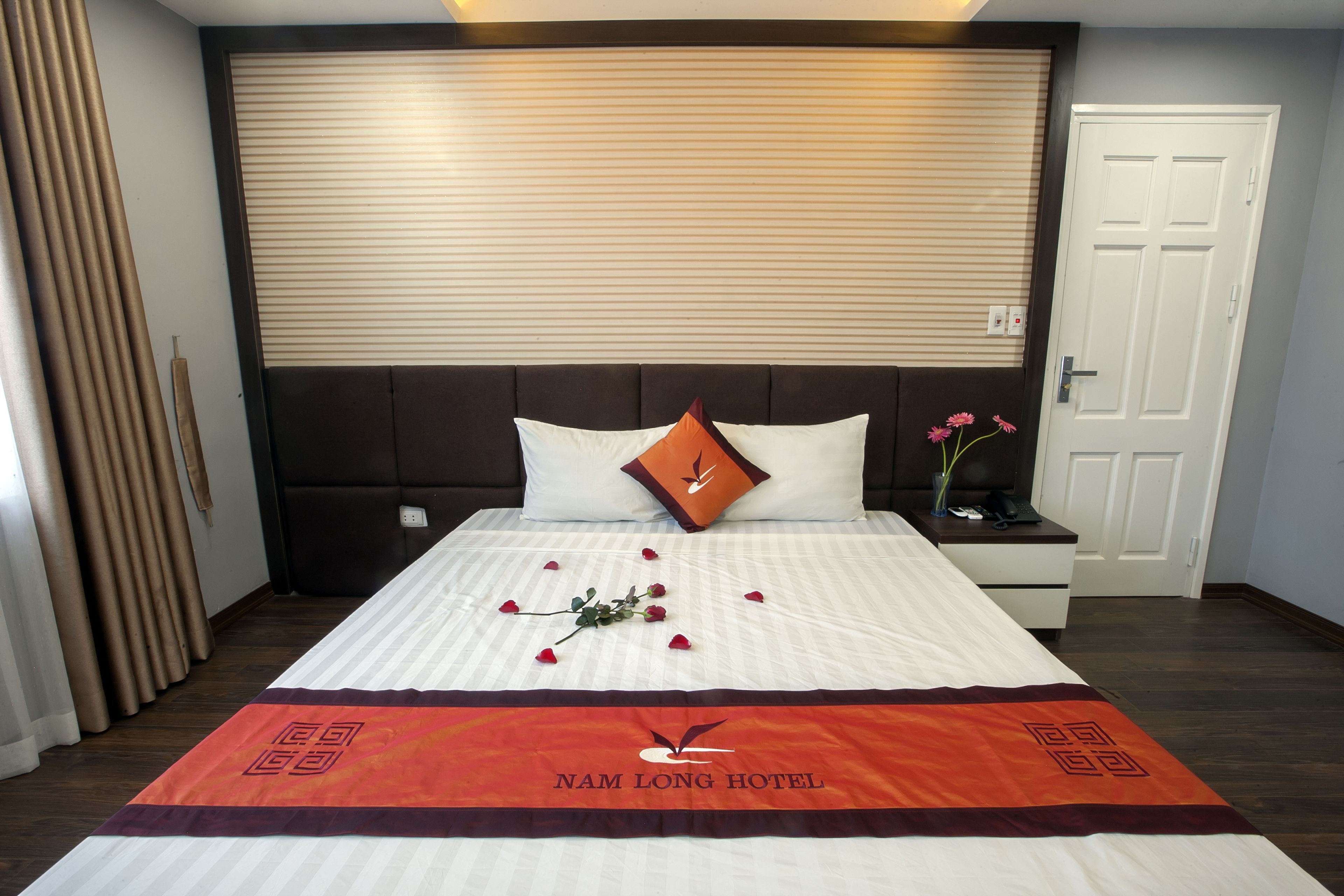 Una habitación de hotel con cama, mesita de noche, persianas y una puerta.