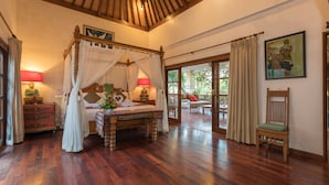 A spacious bedroom with a four-poster bed, wooden flooring, and a large window with curtains. - Villa Kaja by Nagisa Bali (Seminyak)
