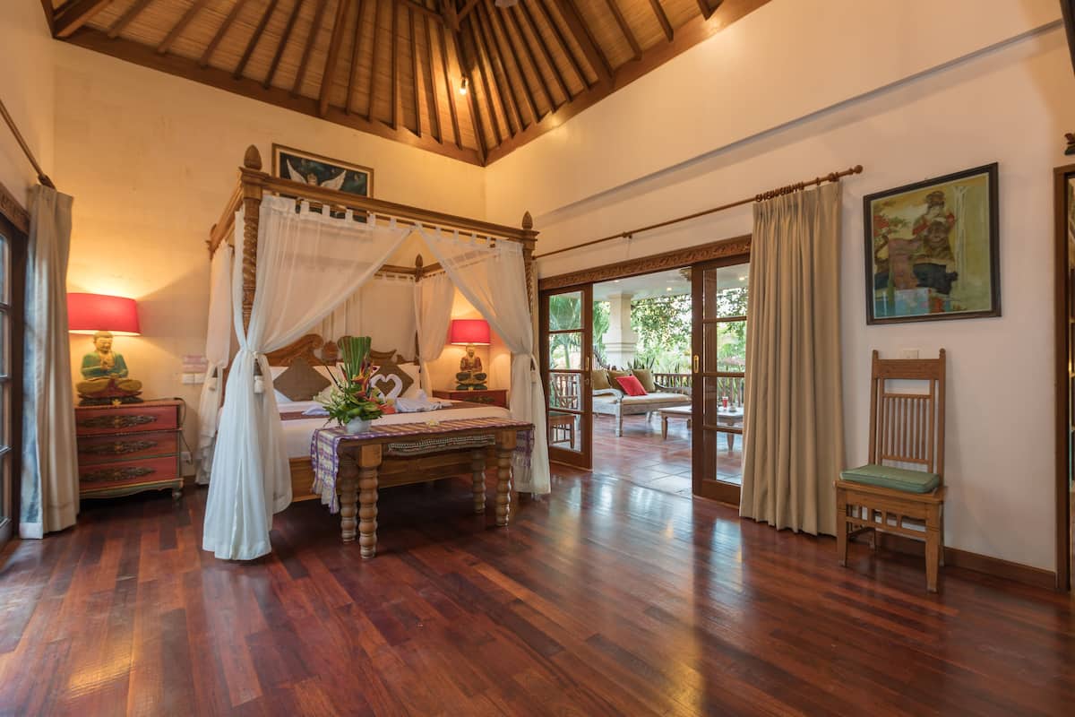 Um quarto espaçoso com uma cama de dossel, piso de madeira e uma janela grande com cortinas.