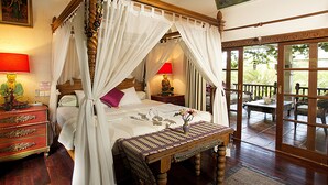 A four-poster bed with white drapes, a wooden bench, and a table with a vase. - Villa Kaja by Nagisa Bali (Seminyak)