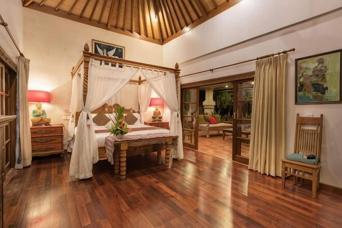 Un lit Ă baldaquin, un plancher en bois, une table de chevet avec une lampe et une chaise.