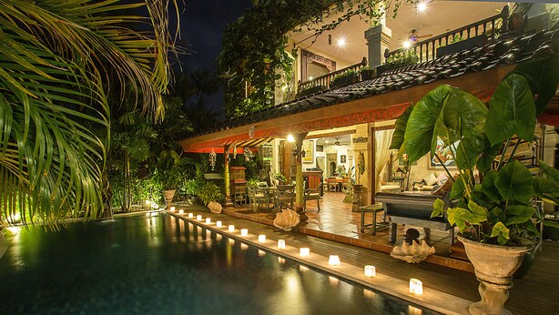 A poolside area with a water feature, potted plants, and a seating area with tables and chairs. - Villa Kaja by Nagisa Bali (Seminyak)