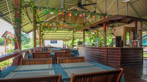 Un restaurant avec des tables et des chaises en bois, un bar et un espace extérieur couvert avec vue sur le paysage environnant.