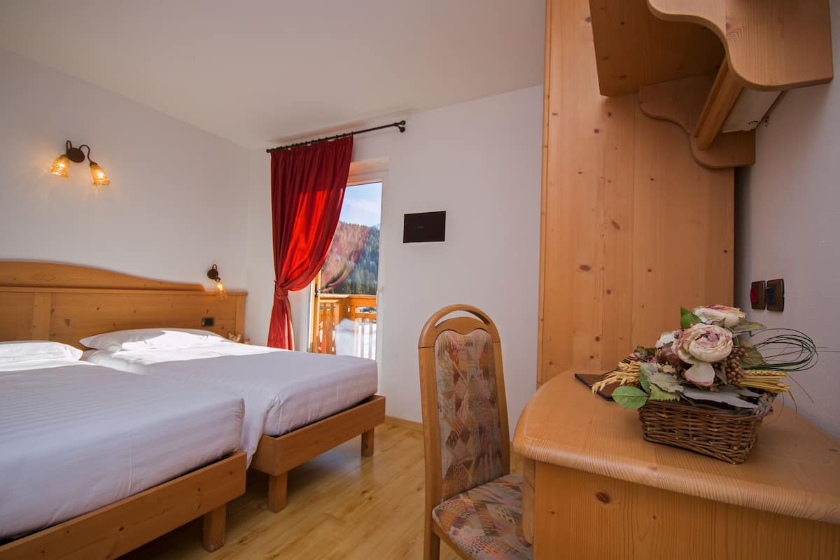 A room with two wooden beds, a chair, a wicker basket with flowers, and a wooden wall unit.