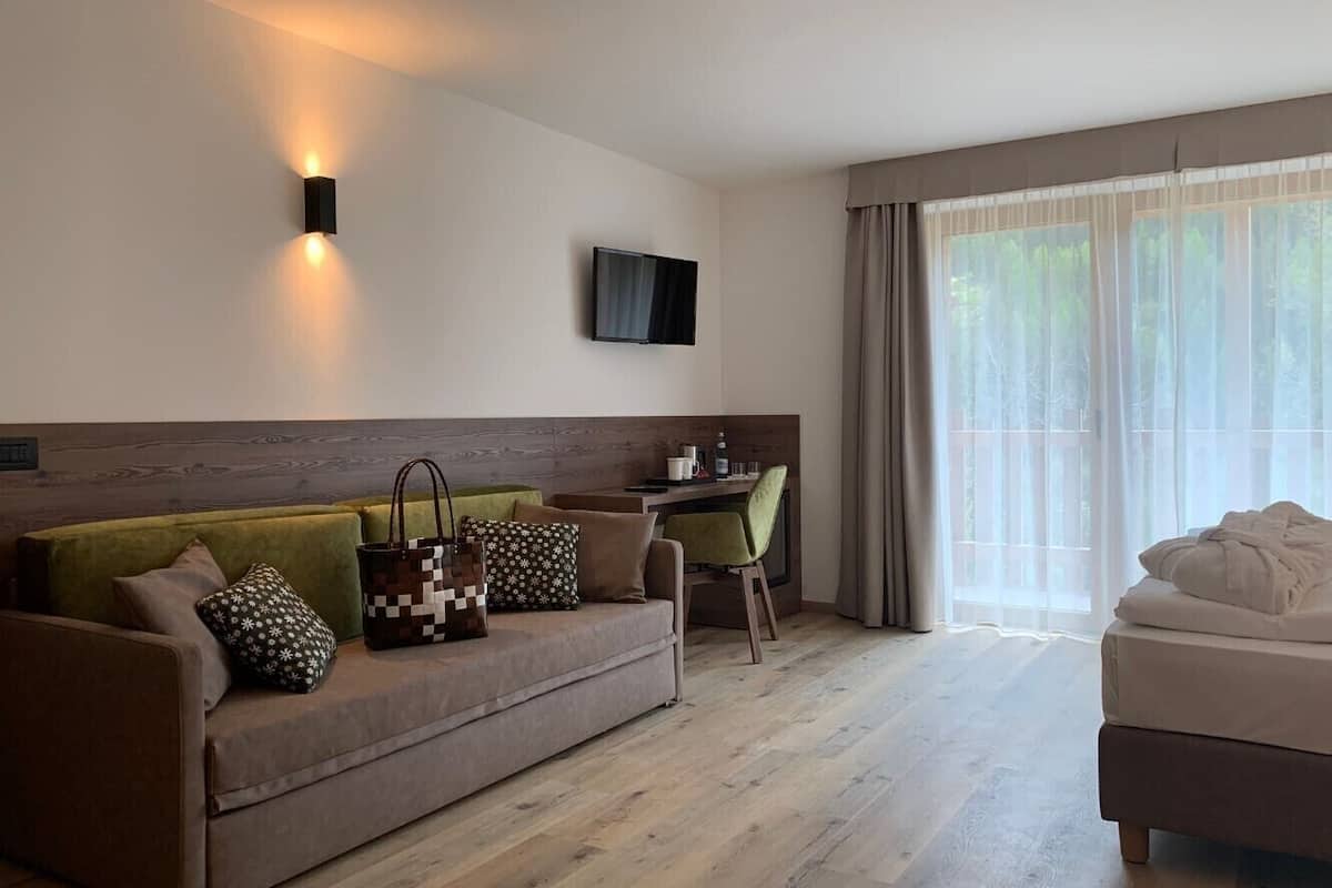 A modern hotel room with a sofa, a small desk, a television, and a large window with curtains.