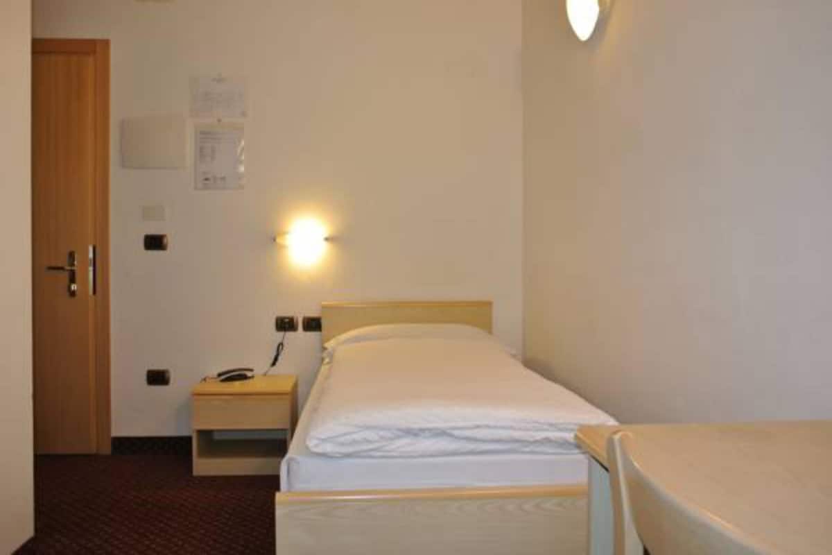 A small, single-bed room with a wooden headboard, a bedside table, and a wall-mounted light.