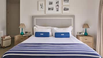 Una cama bien hecha con una colcha a rayas, dos almohadas con la palabra 'SHH' y un cabecero. Encima de la cama hay cuadros enmarcados en la pared.