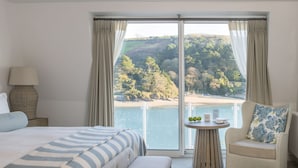 A hotel room with a large bed, a chair, a small table with a view of the sea, and curtains. - Harbour Hotel Salcombe (Salcombe)