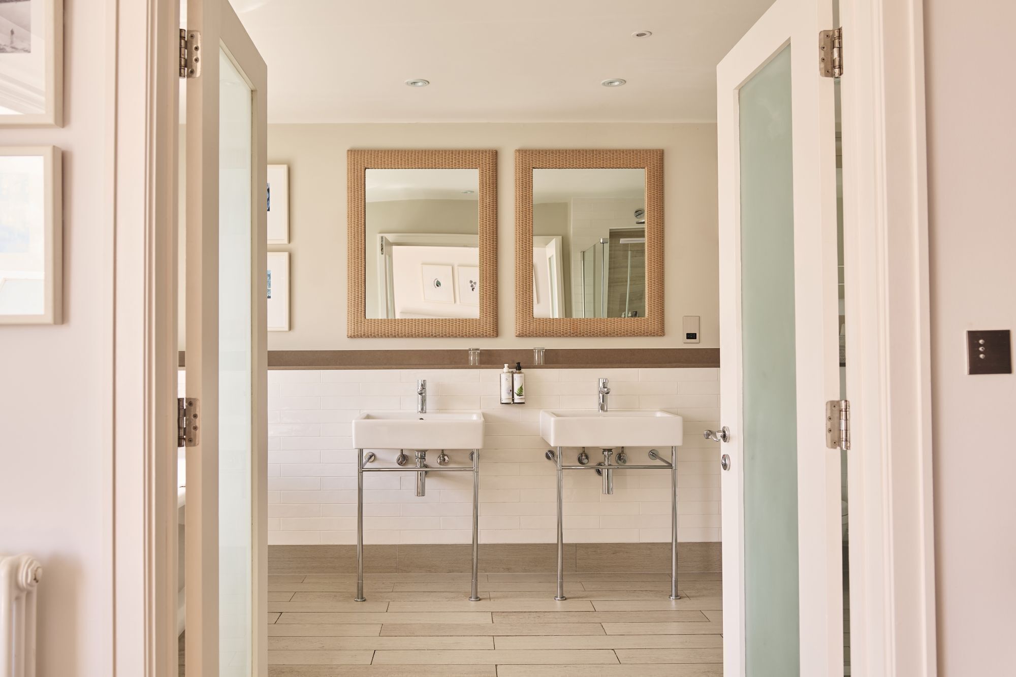 A modern bathroom with two sinks, a mirror, and a light switch on the wall.