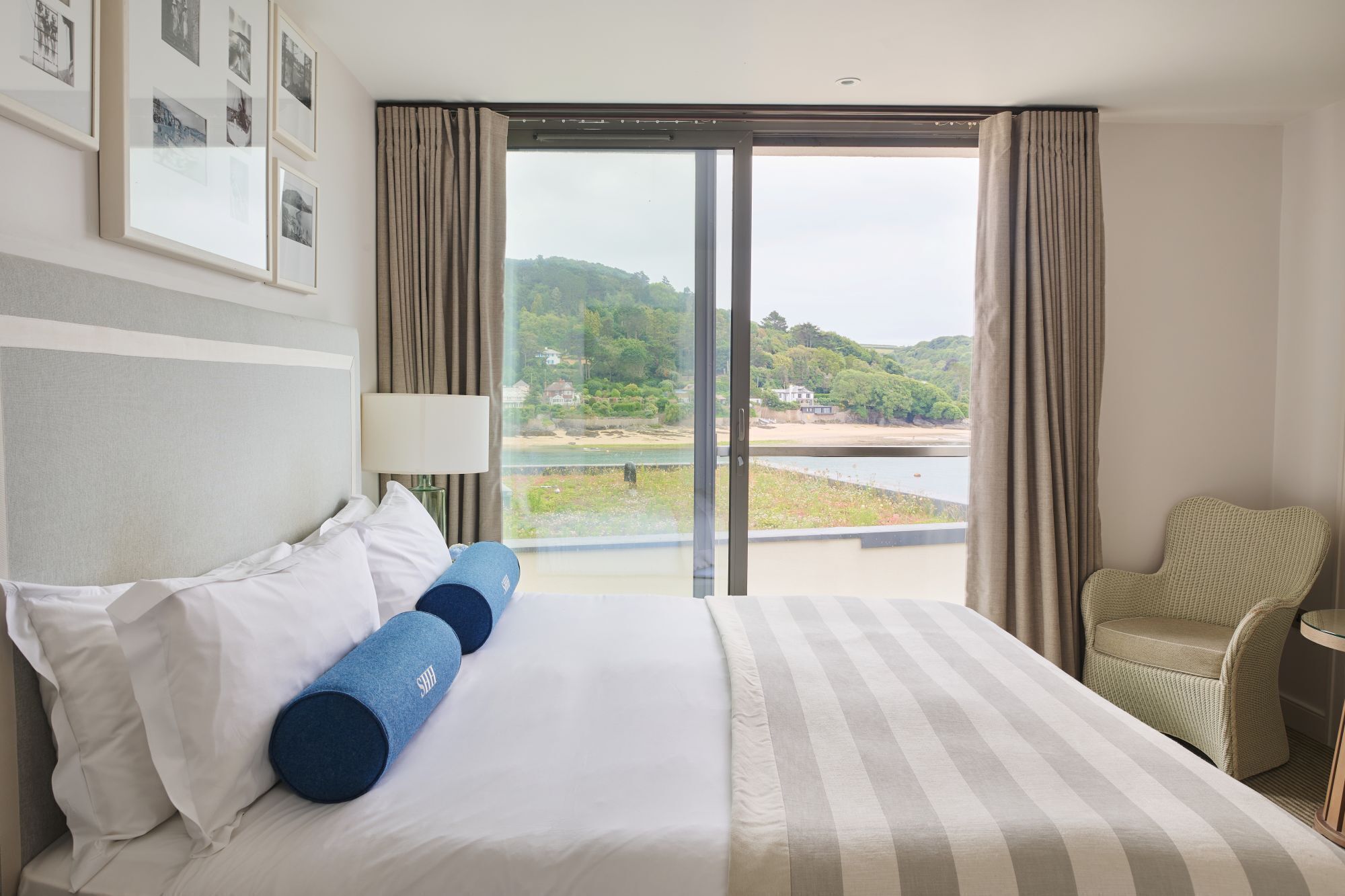 A hotel room with a large bed, a chair, and a view of a lake and hills.