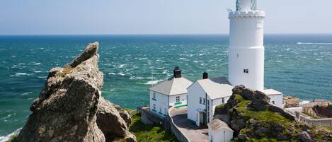 A white lighthouse with a white building adjacent to it, both situated on a rocky coastline with the ocean in the background.