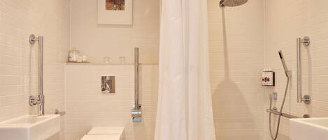 A modern bathroom with a toilet, sink, shower, and a framed picture on the wall.