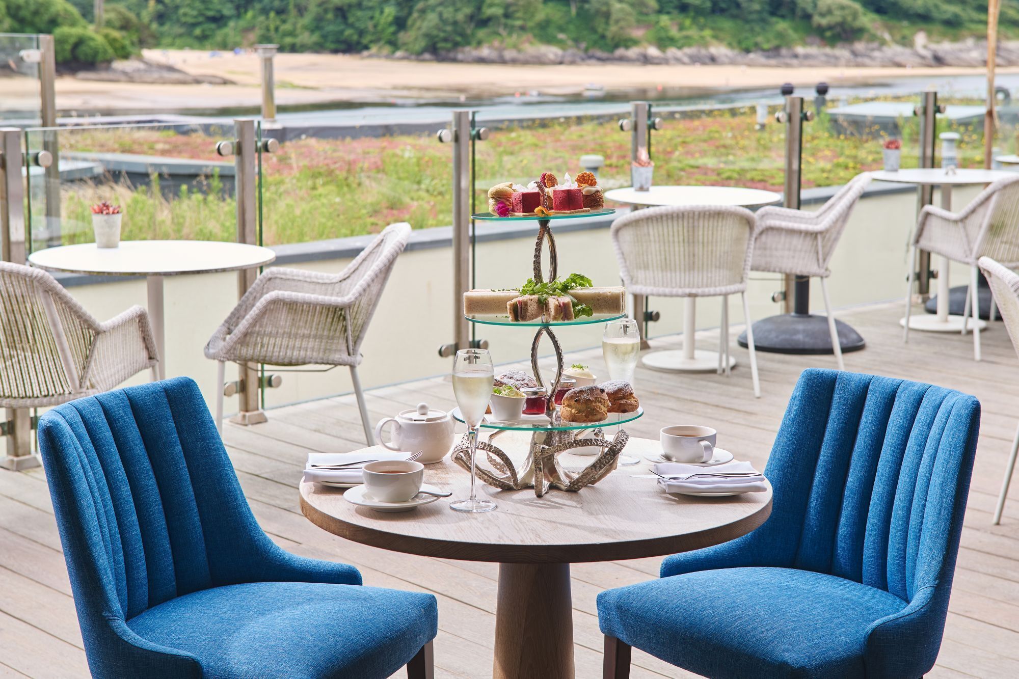 Una terraza con sillones de mimbre, una mesa redonda con un juego de té y un frutero escalonado.
