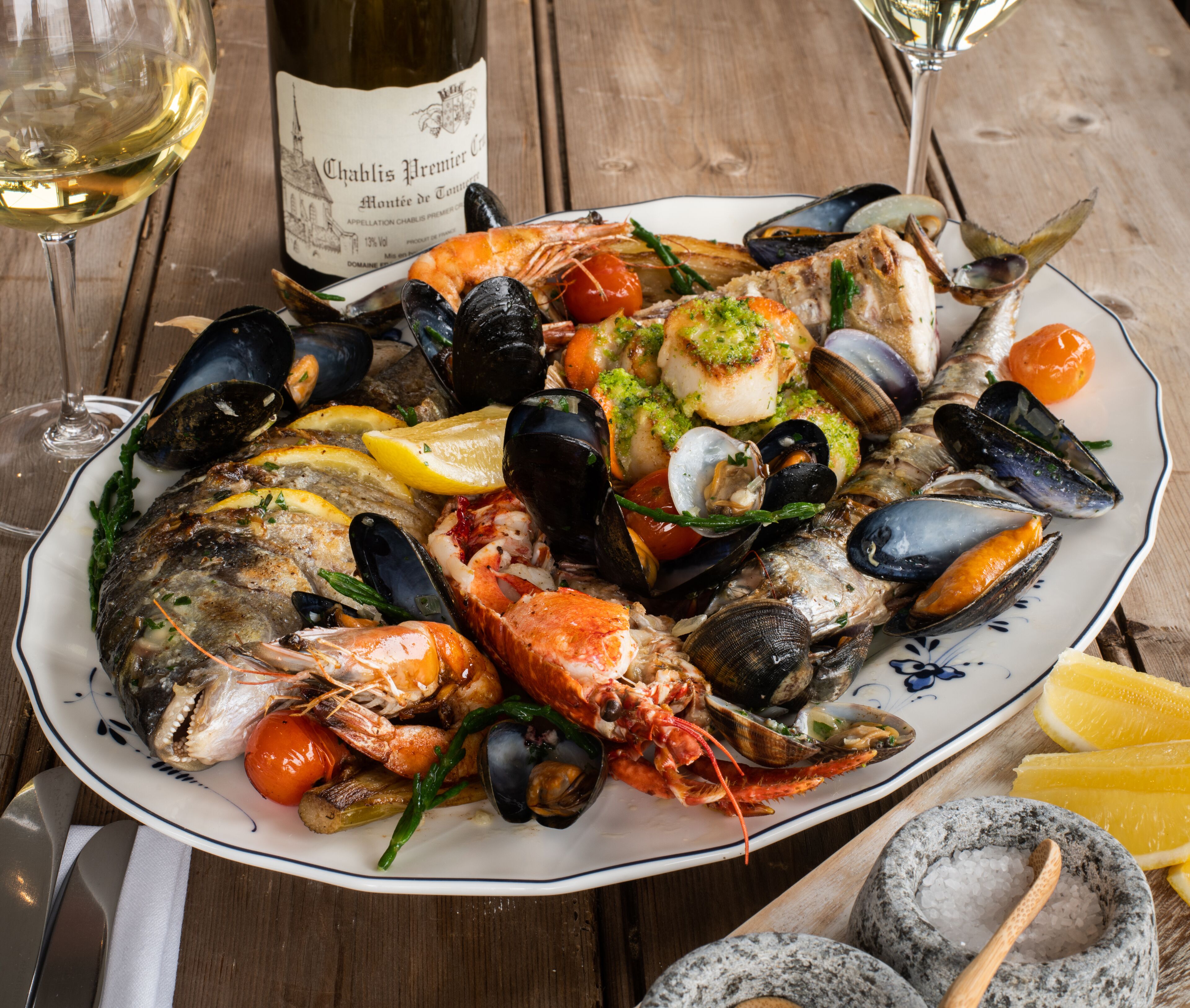 A seafood platter with mussels, shrimp, and fish on a plate, accompanied by a bottle of wine and a glass.