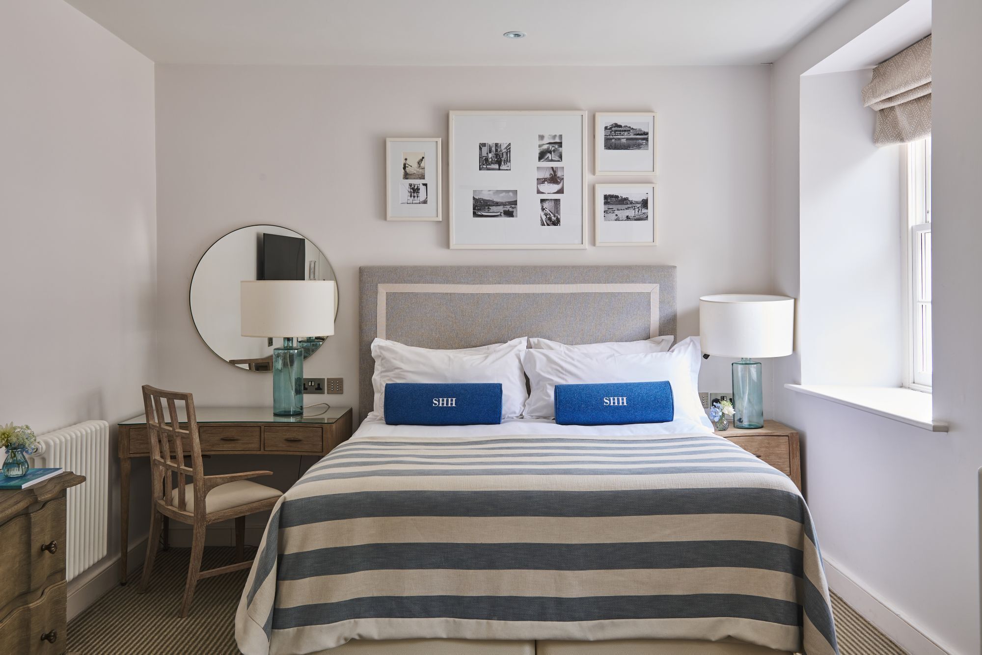 Habitación de hotel con una cama, un espejo redondo, una silla, una mesita y una ventana.