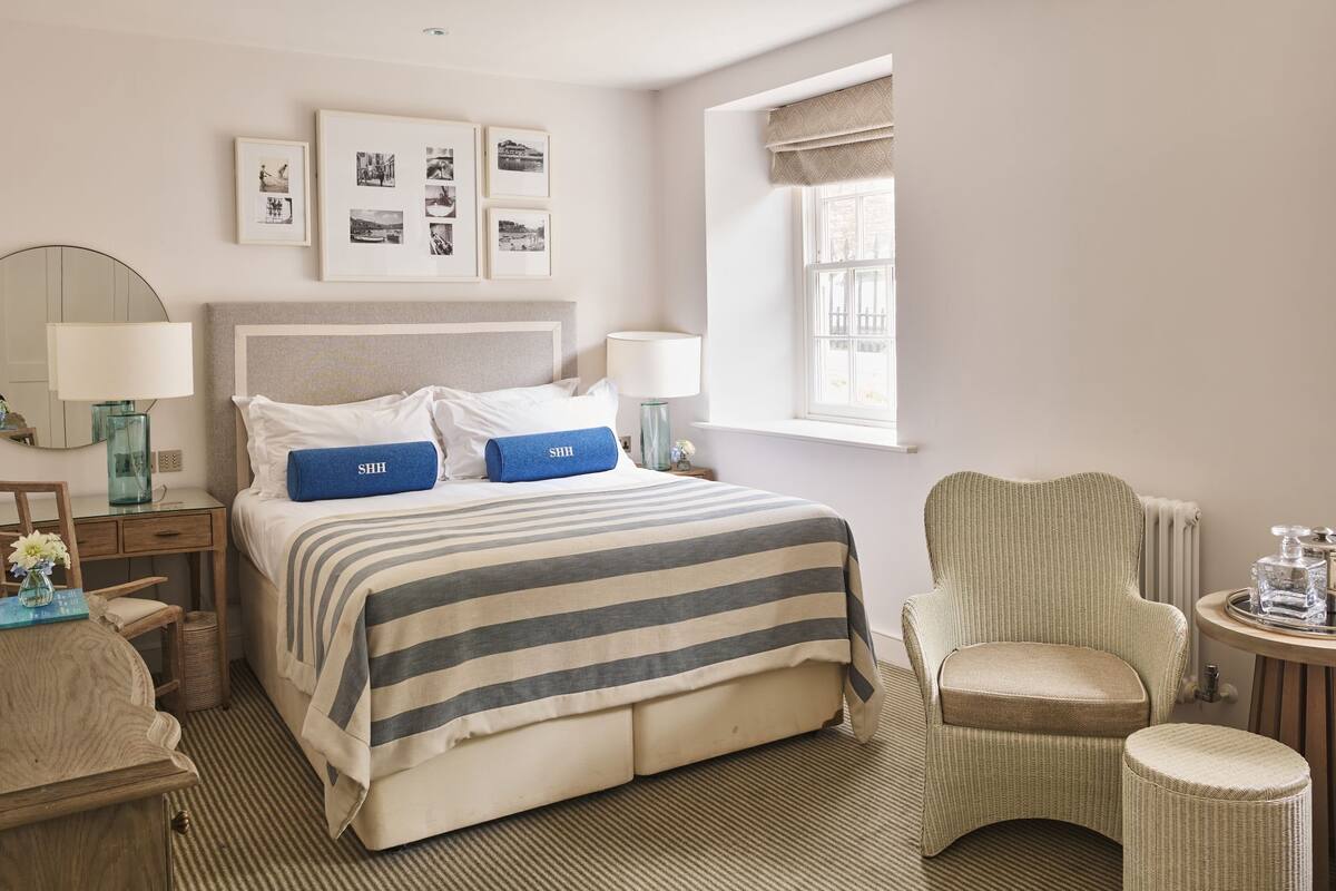 A neatly arranged hotel room with a bed, two bedside tables, a chair, a small table, and a window.