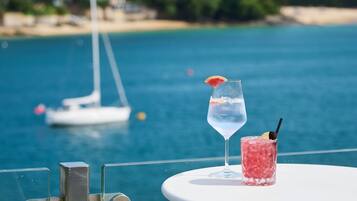 Una mesa con dos bebidas, un vaso de agua y un cóctel rosado, con un velero al fondo.