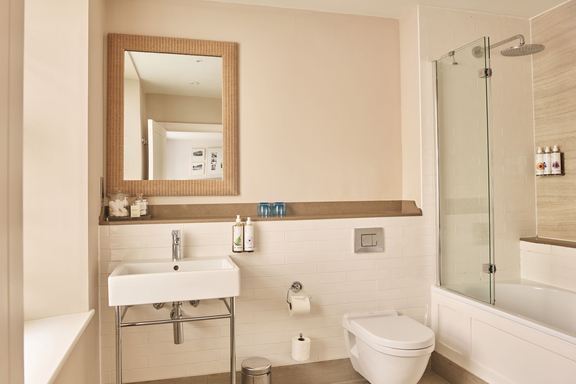 Un baño moderno con lavamanos blanco, espejo, inodoro y ducha con mampara de vidrio.