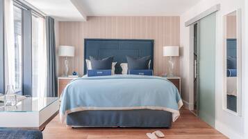 Una habitación de hotel moderna con una cama grande, dos mesitas de noche, una mesa de centro de vidrio y vistas a través de una puerta.