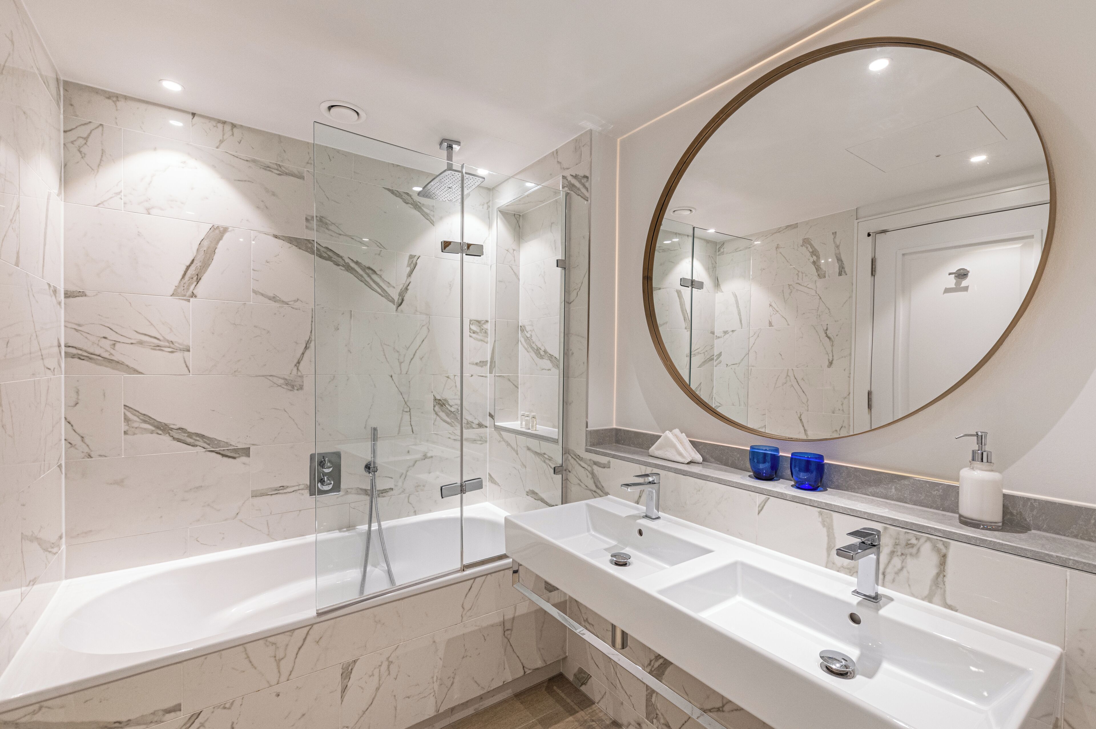 Un baño moderno con ducha de vidrio, un espejo redondo grande y un tocador doble.
