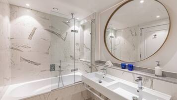 A modern bathroom with a glass-enclosed shower, a large round mirror, and a double sink vanity.