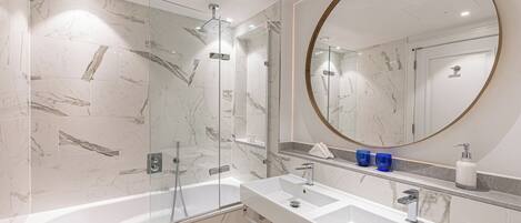Un baño moderno con ducha de vidrio, un espejo redondo grande y un tocador doble.