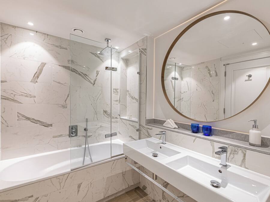 A modern bathroom with a glass-enclosed shower, a large round mirror, and a double sink vanity.