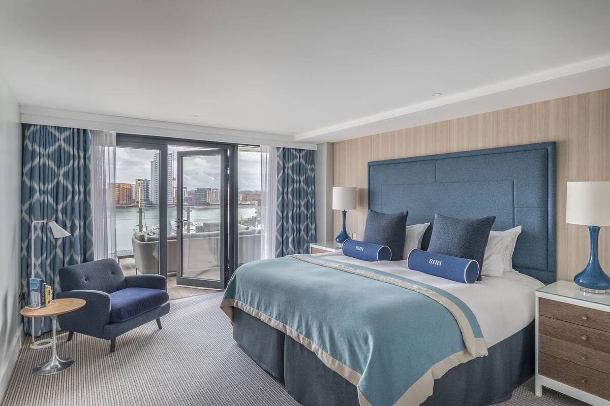 A modern hotel room with a large bed, a seating area, and a view of the city.