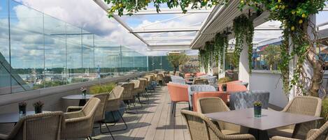 Une terrasse sur le toit, aménagée avec des meubles en osier, des murs en verre et des plantes suspendues.