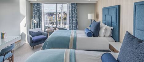 A hotel room with two beds, a desk, a chair, and a view of the marina.