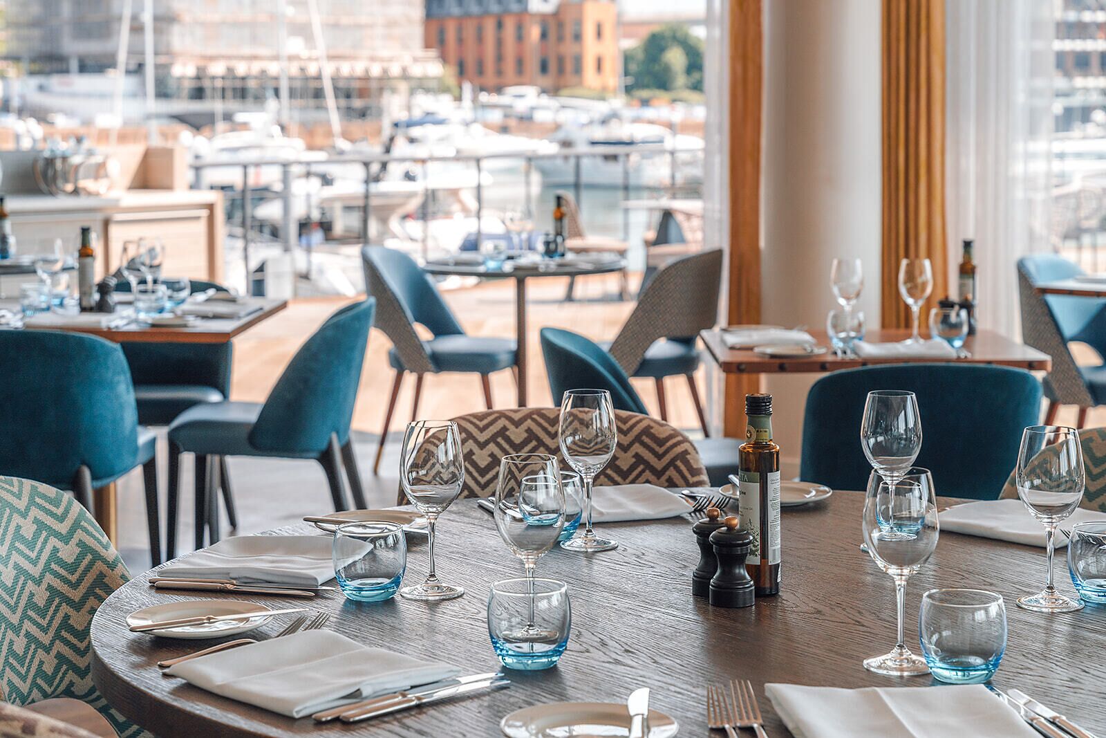 Een restaurant met gedekte tafels, stoelen en uitzicht op boten door grote ramen.