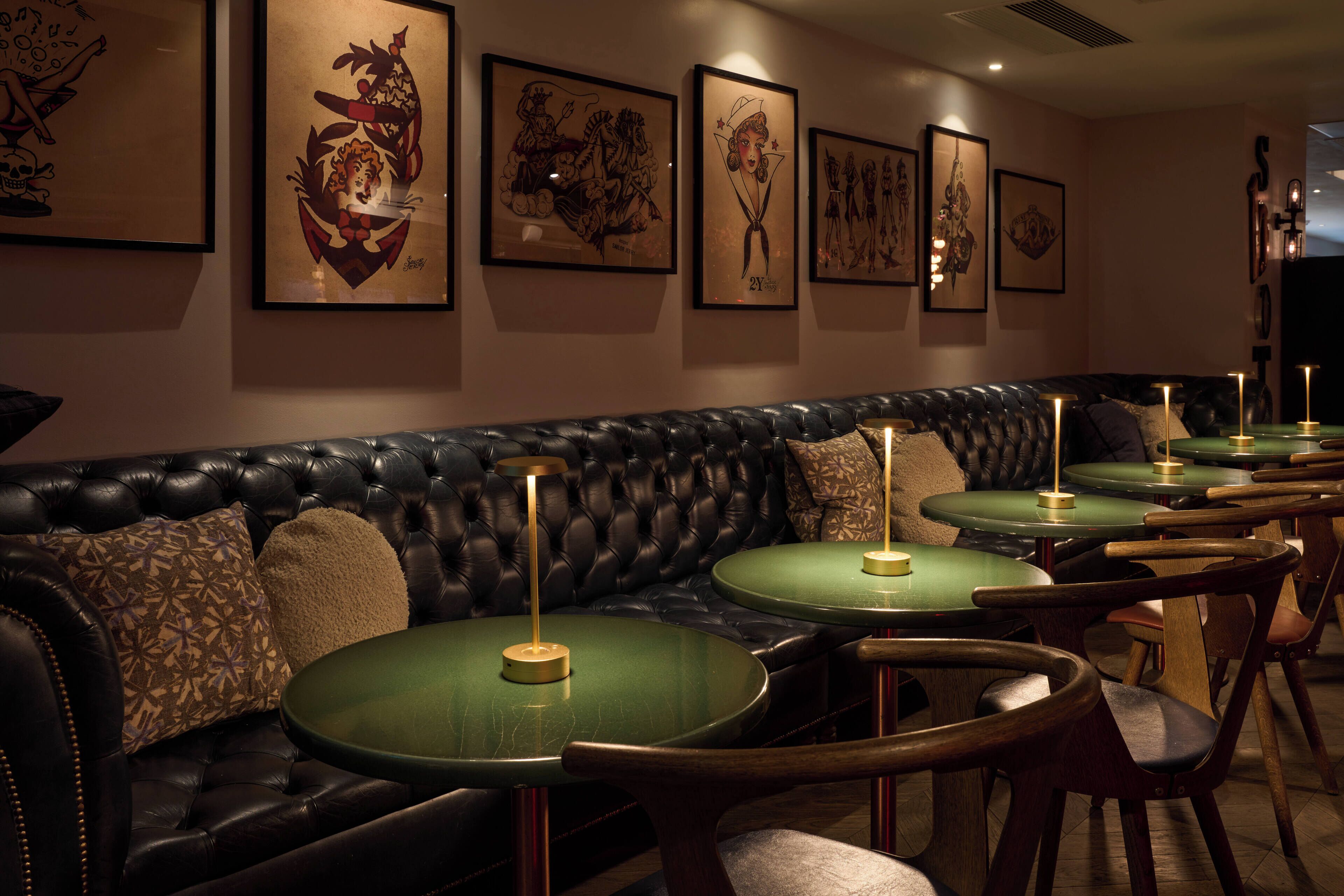 Un restaurant avec des banquettes en cuir noir et des tables rondes dont les plateaux sont verts.