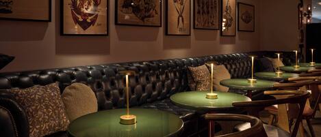 Un restaurant avec des banquettes en cuir noir et des tables rondes dont les plateaux sont verts.