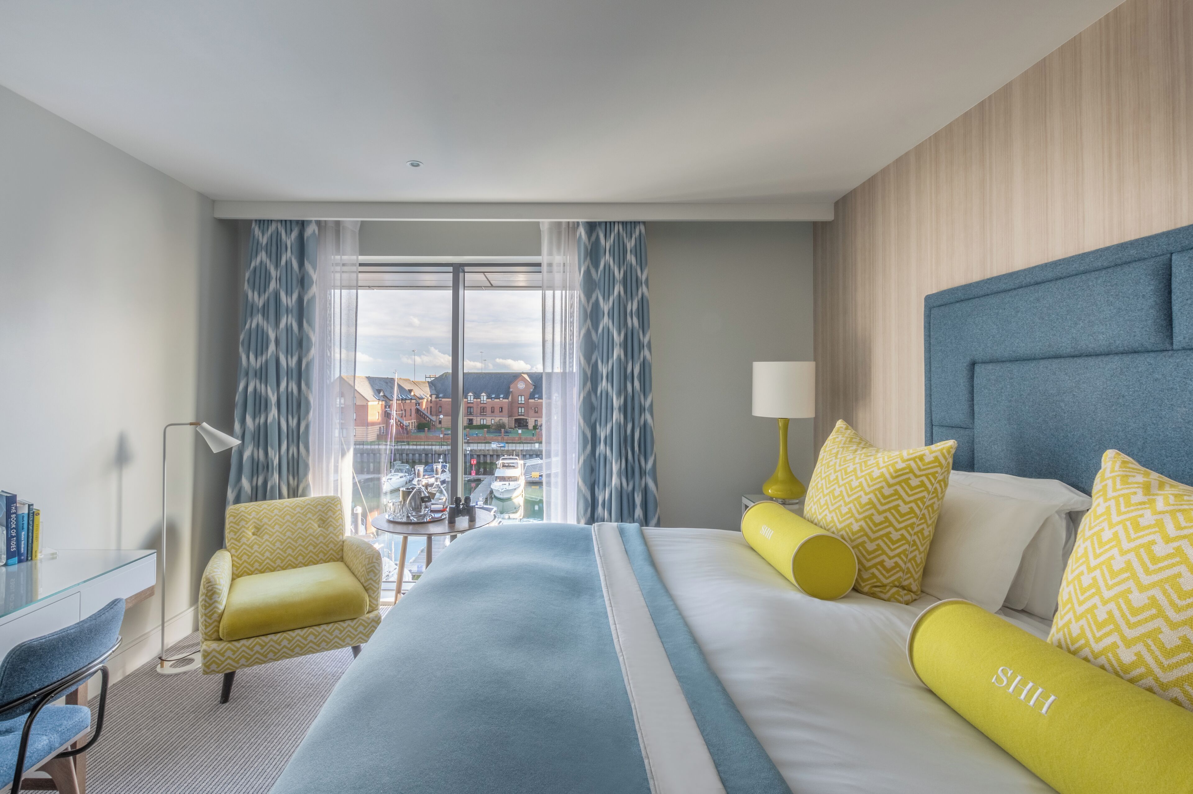 A hotel room with a large bed, a desk, a chair, and a view of the city through the window.