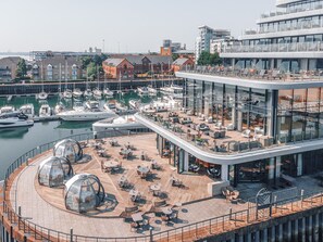 A marina with boats docked, a modern building with outdoor seating, and a glass-enclosed area. - Harbour Hotel Southampton (Southampton)