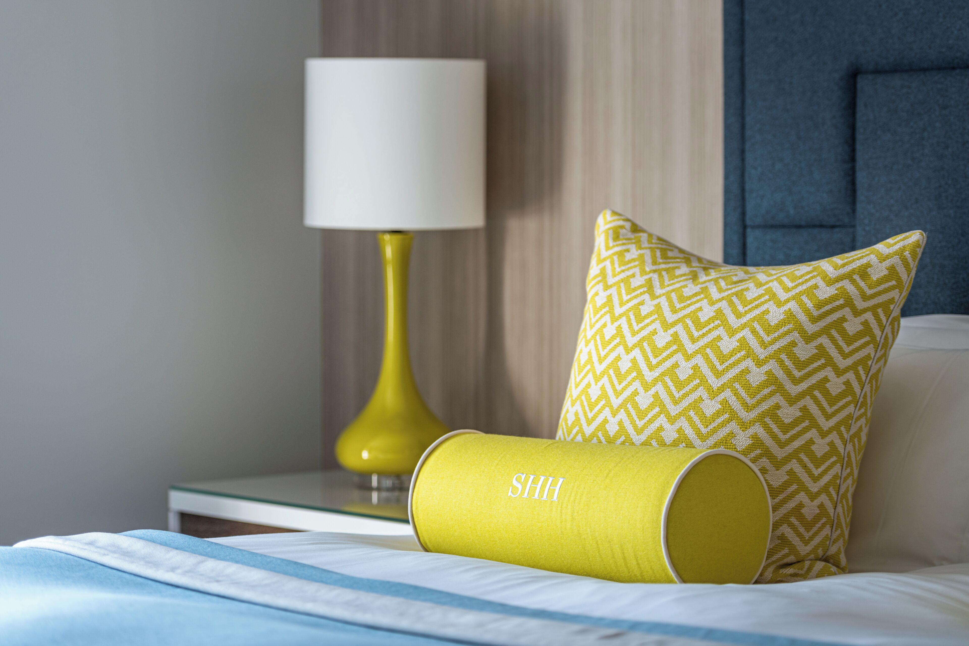 Un lit bien fait, avec un oreiller à motifs et un objet cylindrique jaune portant l’inscription « SHH ».