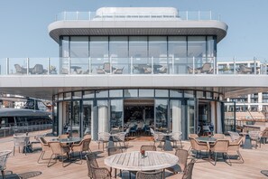 Un edificio moderno con fachada de vidrio y zona de estar al aire libre con mobiliario de mimbre.