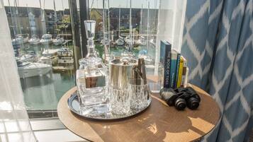 A table with a tray of glassware, a decanter, and books, overlooking a marina with boats.