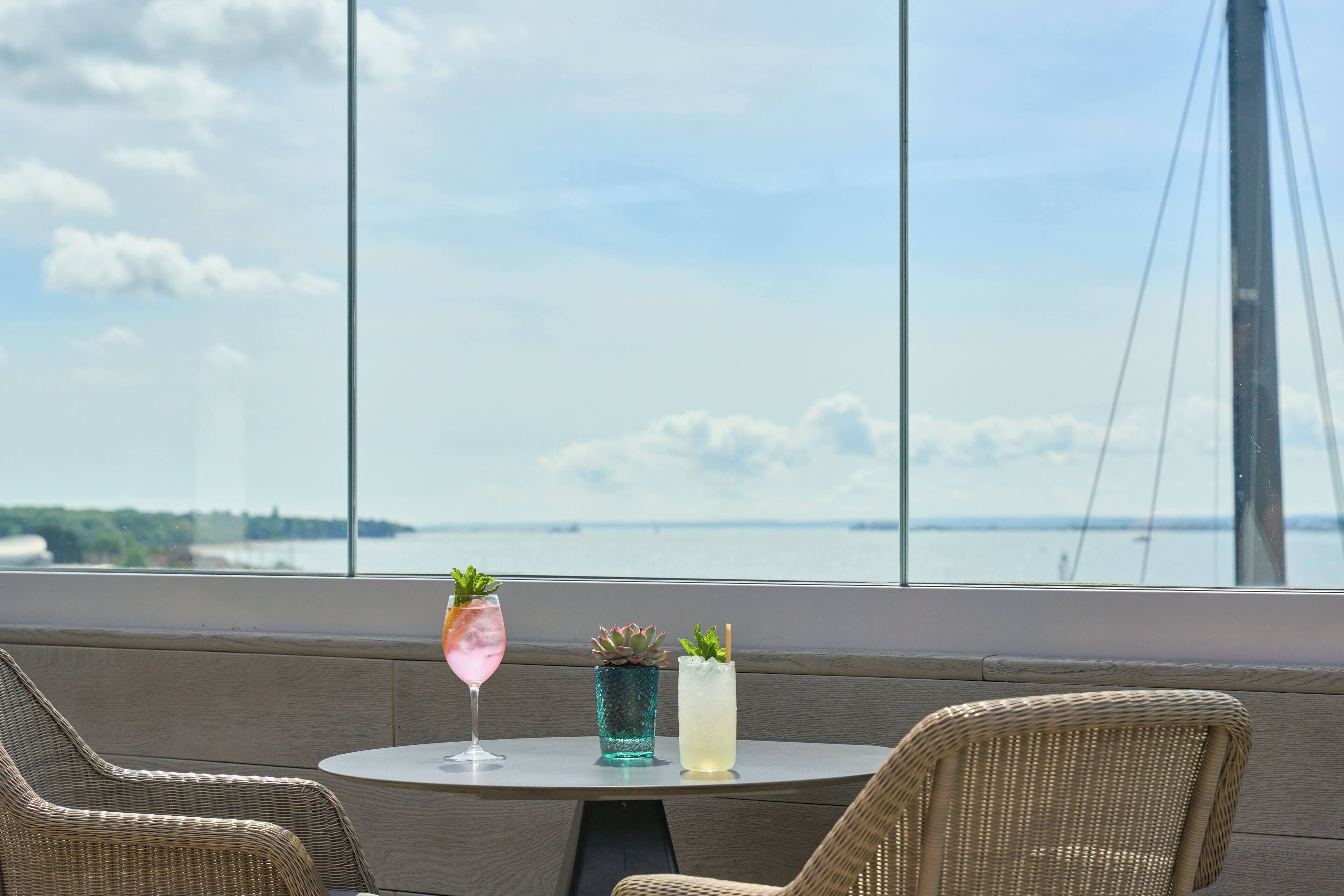 Une table avec deux boissons et une petite plante, donnant sur une étendue d’eau et un pont.
