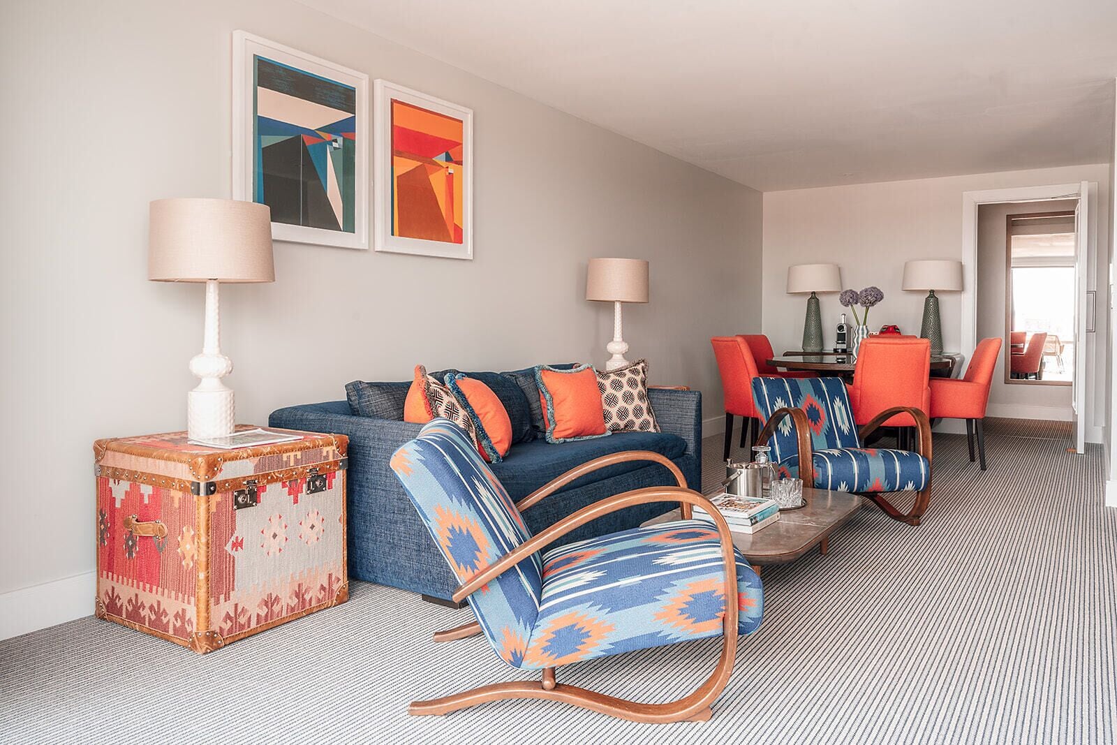 Una sala moderna con un sofá azul, sillones estampados y un comedor con sillas rojas.
