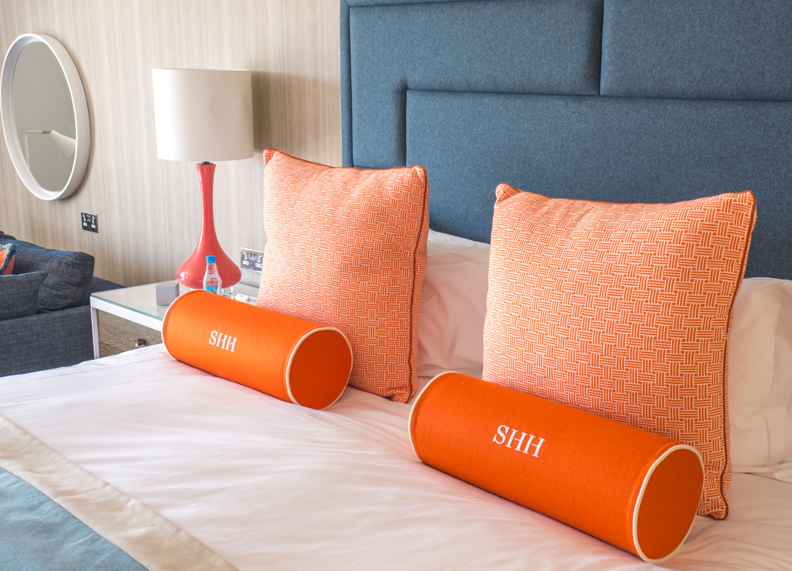 Una cama bien hecha con dos almohadas naranjas y una lámpara roja sobre una mesita de noche.