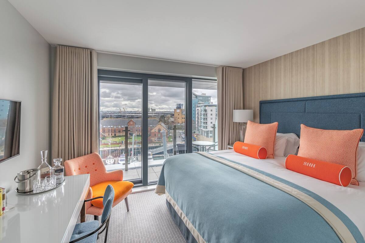 A hotel room with a large bed, a dining table, and a view of the cityscape through the window.