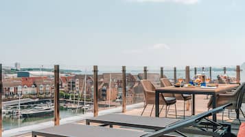 A terrace with a table set for dining, overlooking a marina with boats and buildings.
