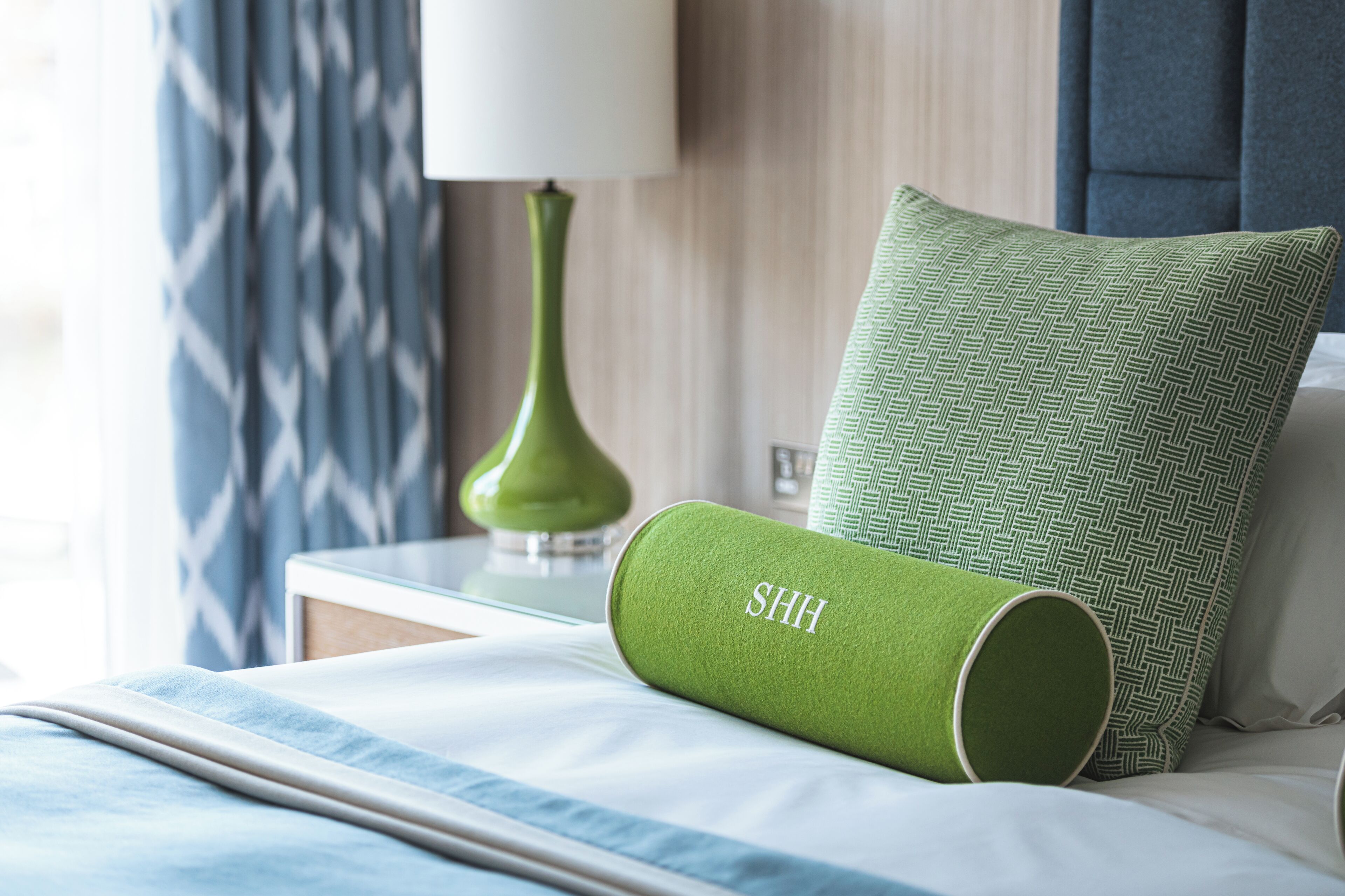 A neatly made bed with a green pillow and a green cylindrical object with "SHH" on it.