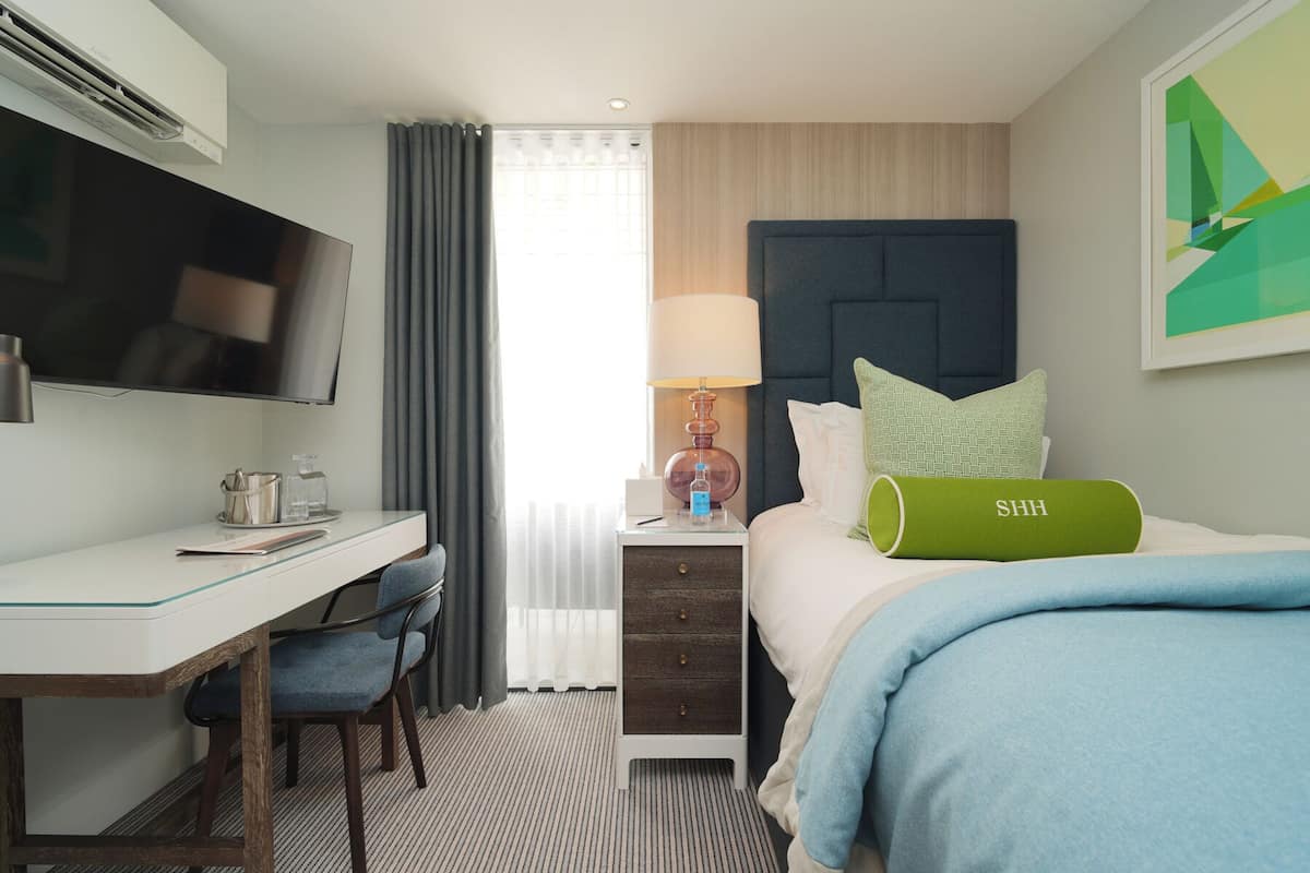 A hotel room with a bed, a desk, a TV, a lamp, and a window with curtains.