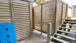 Una cancelada de madera con listones horizontales, un felpudo azul con agujeros y una escalera de madera.