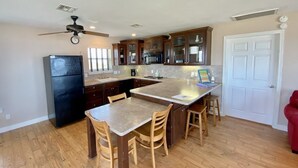 Una cocina con armarios de madera, un refrigerador negro, una mesa de comedor con sillas y un ventilador de techo.